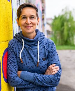 Barbara Andrä in blauen Pullover vor einer Wand mit Grafiti.